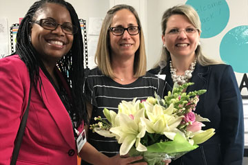 2018 Teacher of the Year holding flowers with superintendent and principal