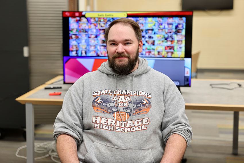 Librarian in Heritage HS shirt sitting in front of video game monitor