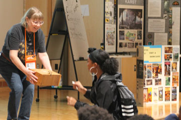 Cave expert holding box on stage with student approaching