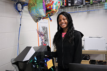 Student smiling standing next to computer and balloons