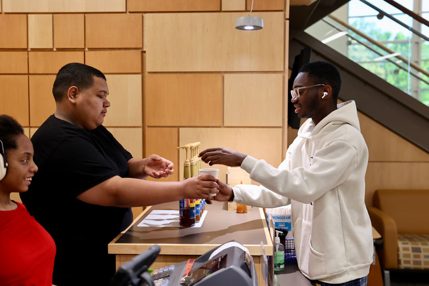 Student handing coffee to another student in cafe