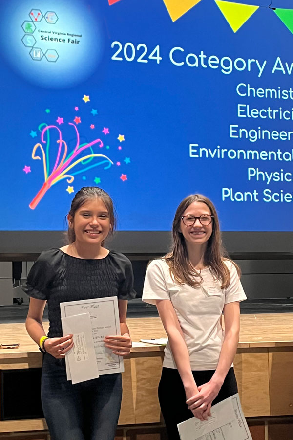 Two students holding certificates in front of science fair presentation