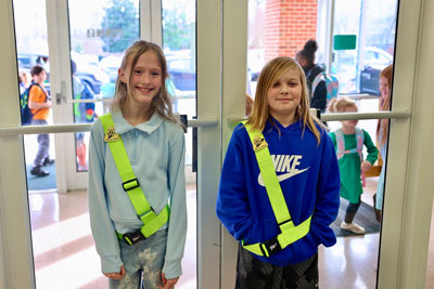 Two students wearing safety patrol belts standing at school entrance