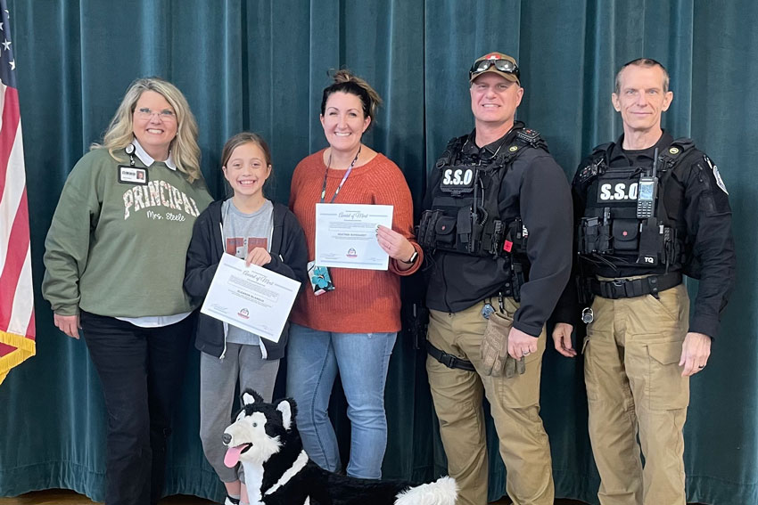 Student and teacher holding certificates with principal and two school security officers